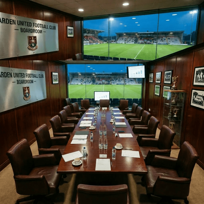 Boardroom meeting of Ardeen United Football Club with executives seated around a long table and stadium visible through large windows.
