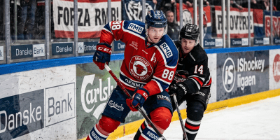 Two ice hockey players battle for the puck near the boards