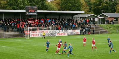 Women’s football match with scoreboard showing 64:23, cheering fans, and Danish banners supporting women’s football